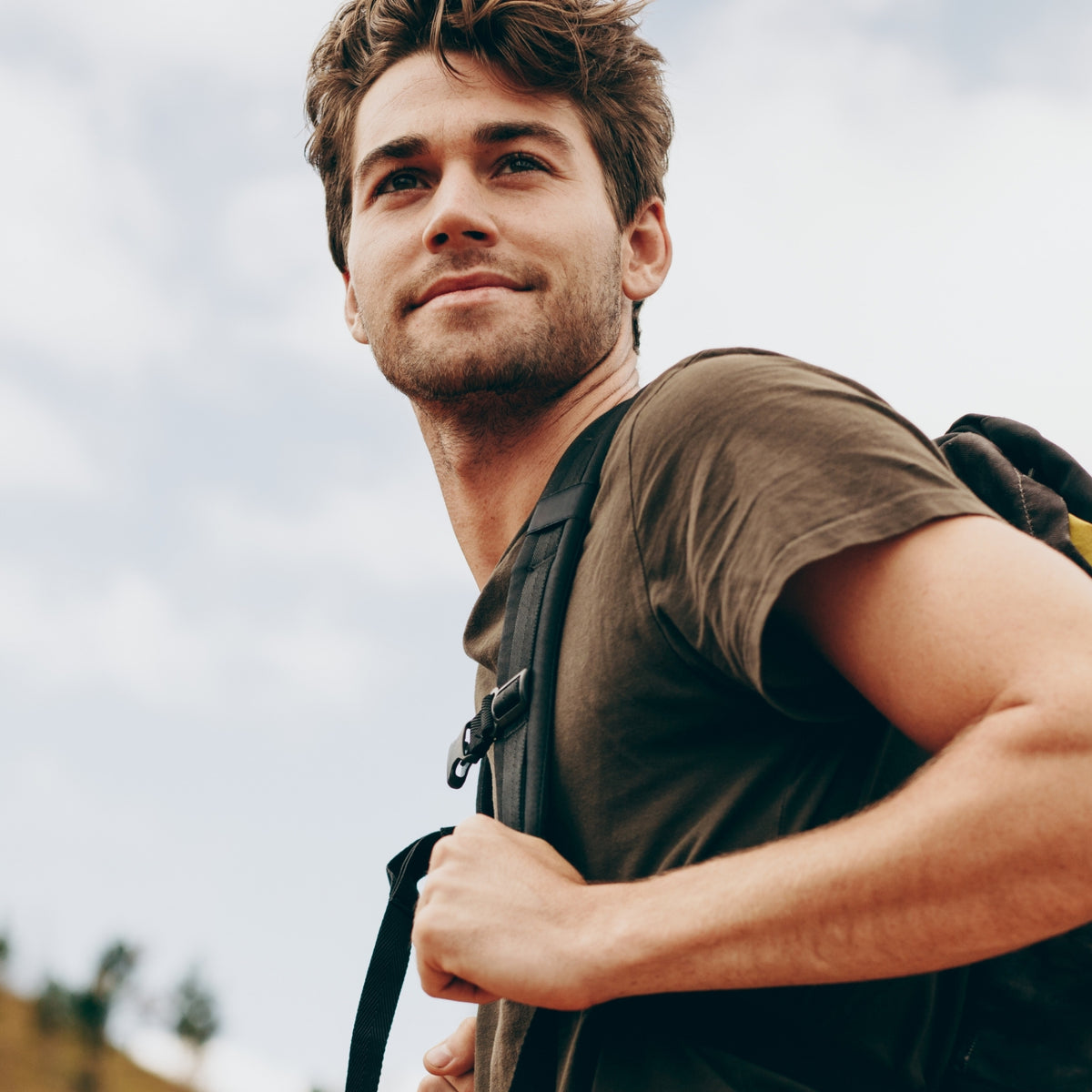 Man with a backpack looking up against a cloudy sky