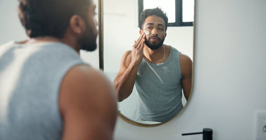 Man in Grey Tank top applying face cream on face in front of a mirror