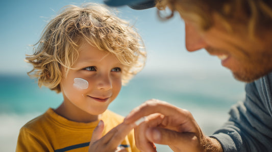 Young blond boy wearing a yellow t-shirt and with sunscreen on his left cheek with his dad on the beach